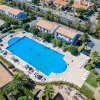 Vista aerea di una grande piscina circondata da lettini, edifici e alberi.