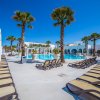 Piscina con palme e ospiti che nuotano, cielo sereno e mare sullo sfondo.