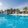Ampia piscina con acqua scintillante, circondata da palme e lettini bianchi.