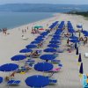 Vista aerea di una spiaggia con ombrelloni colorati e una vegetazione lussureggiante sullo sfondo.