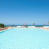Grande piscina con vista sul mare, lettini bianchi e cielo limpido sullo sfondo.